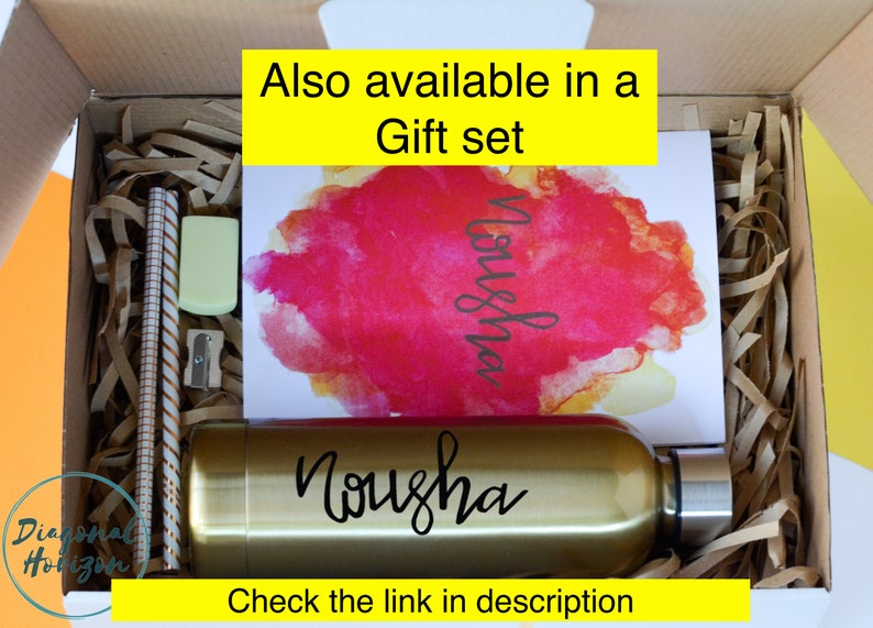 May include: A gift set featuring a gold water bottle with the name "Nousha" on it. The set also includes a card with a watercolour design and the name "Nousha" written on it. The text "Also available in a Gift set" is at the top of the image.