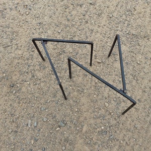 May include: Three black metal frames are arranged in a triangular shape on a gravel surface. The frames are made of thin metal and are connected at the corners.