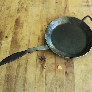 May include: A vintage cast iron pan with a long, curved handle. The pan is dark gray and has a rustic look.