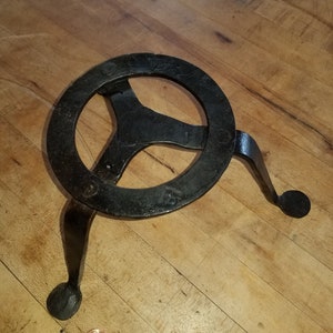 May include: A black metal trivet with a circular top and three legs. The trivet is designed to protect surfaces from hot pots and pans.