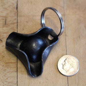 May include: A black metal key chain with a three-pointed design and a silver ring. The key chain has a smooth, rounded surface.