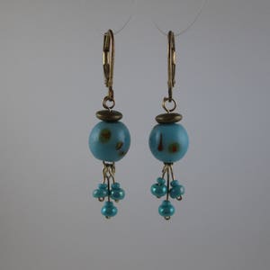 May include: A pair of blue and gold earrings with a large blue bead and smaller blue beads dangling below. The large bead has a gold accent and a subtle pattern.