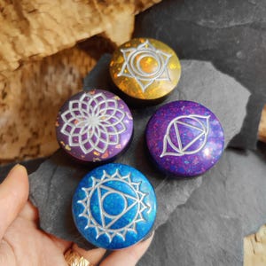 Puede incluir: Cuatro piedras de chakra redondas, coloridas, de resina con símbolos plateados. Cada piedra tiene un color y un símbolo diferentes que representan un chakra diferente.