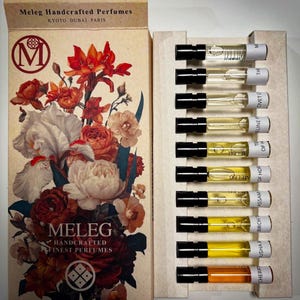 Può includere: Un set di campioni di profumo Meleg. La scatola presenta un design floreale con rose e iris. Il set include una varietà di fiale di profumo con tappi neri. Il testo sulla scatola recita "Meleg Handcrafted Finest Perfumes, Kyoto Dubai Paris."