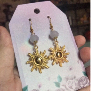 May include: A pair of gold sun earrings with a light gray bead on each earring.