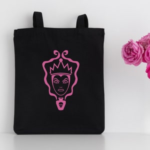 May include: Black tote bag with a pink silhouette of the Evil Queen from Snow White. The Evil Queen is wearing a crown and holding a poisoned apple.