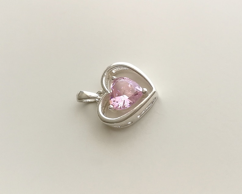 Peut inclure: Pendentif en argent en forme de c&oelig;ur avec une pierre pr&eacute;cieuse rose. Le pendentif pr&eacute;sente un design d&eacute;licat et ouvert, mettant en valeur la pierre pr&eacute;cieuse en forme de c&oelig;ur. La pierre est rose clair, ajoutant une touche d'&eacute;l&eacute;gance.