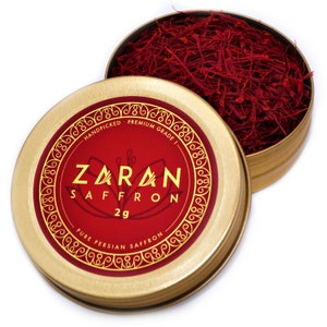 May include: A gold tin with a red label that says "Zaran Saffron 2g - Handpicked - Premium Grade - Pure Persian Saffron" and contains red saffron threads.