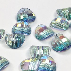 May include: A group of iridescent blue and green glass beads in the shape of half-hearts. The beads have a faceted design and are scattered on a white surface.