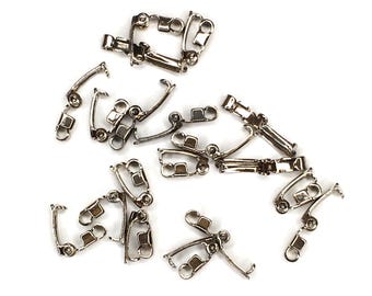 May include: A collection of silver-toned metal earring findings, specifically clip-on earring converters with a hinged mechanism and a small loop at the bottom for attaching charms or dangles, scattered across a plain white surface.