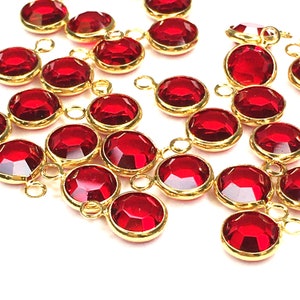 May include: A group of red crystal beads with gold-toned metal loops. The beads are round and have a faceted design.