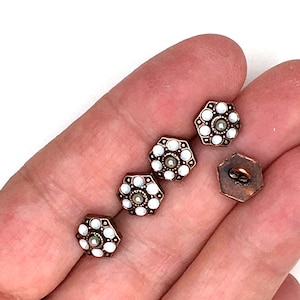 May include: A selection of antique buttons. The buttons have a hexagonal shape with a bronze-coloured metal frame. Each button features a central pearl-like bead surrounded by white, pearl-like beads. The buttons are displayed on a light background.