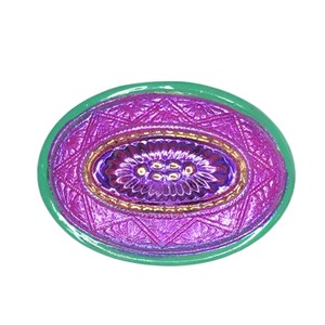 May include: An oval-shaped, decorative object with a green border. The center features a textured, purple design with gold accents. The design includes floral and geometric patterns, creating a vintage or antique aesthetic.