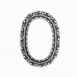 May include: A silver oval picture frame with an ornate design. The frame has a raised edge and a smooth finish.
