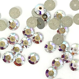 May include: A scattering of iridescent clear glass rhinestones, some with a silver backing, on a white surface.