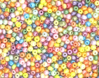 May include: A large assortment of colorful seed beads in various pastel shades, including pink, blue, yellow, green, and purple. The beads are small and round, with a smooth, shiny finish.