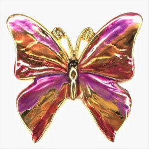May include: A gold-tone butterfly brooch with iridescent pink and orange wings. The butterfly has a black center with a gold outline.