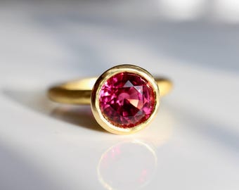 Puede incluir: Un anillo de oro con una piedra preciosa rosa engastada en un engaste de bisel.