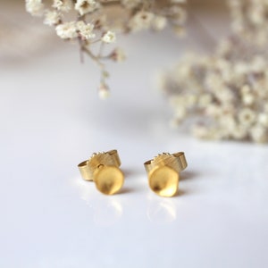 May include: A pair of gold-toned earrings with a textured, slightly rounded, petal-like design.