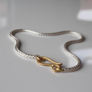 May include: A silver chain bracelet with a gold hook clasp. The chain is braided and has a polished finish.