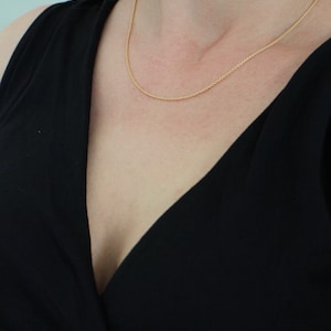 May include: A close-up of a woman wearing a black v-neck top with a thin gold chain necklace.