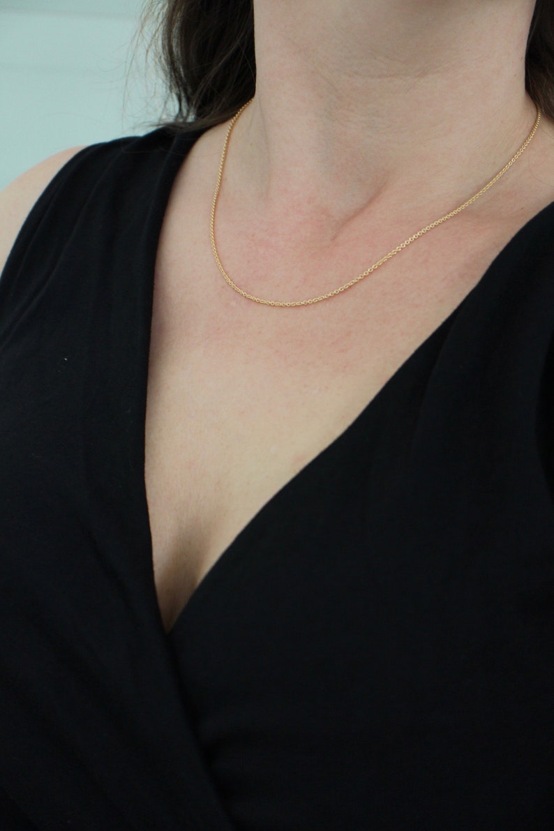 May include: A close-up of a woman wearing a black v-neck top with a thin gold chain necklace.