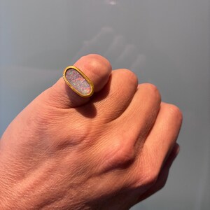 May include: An oval-shaped ring featuring a bezel-set opal gemstone with iridescent flashes of color. The stone is encased in a smooth, polished yellow gold band that follows the elongated oval contour of the central setting.