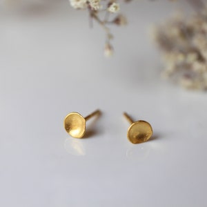 May include: A pair of gold-toned stud earrings with a slightly rounded, textured, disc-shaped design.