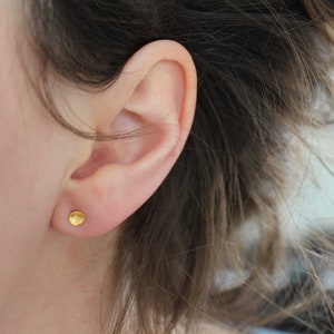 May include: A close-up of a person's ear with a small, round, gold earring.