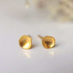 May include: A pair of small, gold-toned earrings with a textured, rounded shape. The earrings are simple and delicate.