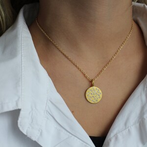 May include: A gold chain necklace with a round pendant featuring a pattern of small, white diamonds.