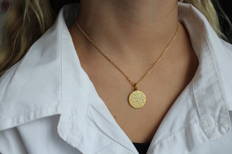 May include: A gold chain necklace with a round pendant featuring a pattern of small, white diamonds.