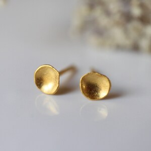 May include: A pair of gold-toned stud earrings with a rounded, slightly concave shape. The earrings have a smooth, brushed finish.