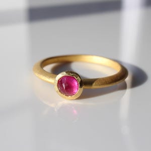 Puede incluir: Un anillo de oro con una piedra preciosa rosa engastada.