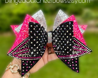 May include: A large, sparkly cheer bow with a black base, white polka dots, and pink and silver accents. The bow is embellished with rhinestones and has a rhinestone center. The text "BlingedOutCheerBows.etsy.com" is visible.