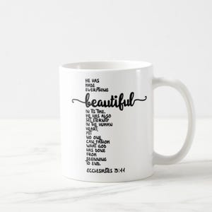 May include: White ceramic coffee mug with a curved handle. The mug features black script that reads "He has made everything beautiful" and a Bible verse from Ecclesiastes 3:11.
