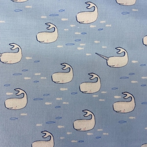 May include: A light blue fabric with a repeating pattern of white whales and small fish. The whales are in various positions, some with their mouths open and some with their tails up. The fish are scattered throughout the fabric.