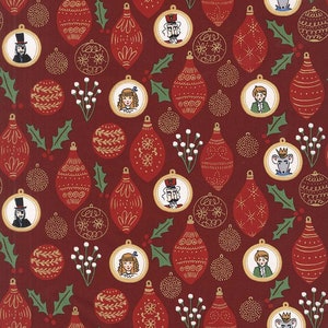 Op de afbeelding: Rode stof met een herhalend patroon van kerstballen, hulstbladeren en kleine witte bloemen. De kerstballen zijn versierd met gouden details en bevatten afbeeldingen van personages uit het verhaal van de Notenkraker.