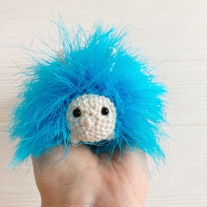 May include: A small crocheted toy with a white body and blue fur. The toy has black eyes and a small, round nose.