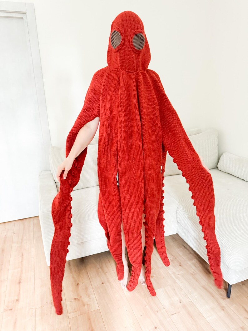 May include: A vibrant red octopus costume. The hooded garment features large, round eye openings and eight long, tentacle-like appendages. The tentacles have small, round details. The costume is made of a knitted material.