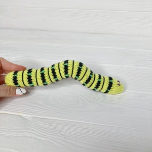 May include: A yellow and black striped knitted snake toy with green accents and purple eyes.