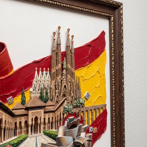 Può includere: Un'opera d'arte incorniciata raffigurante monumenti spagnoli, tra cui la Sagrada Familia e il Museo Guggenheim, su sfondo di bandiera rossa e gialla. La parola "SPAIN" è scritta in un carattere decorativo.