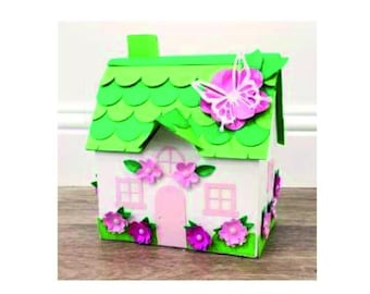 May include: A small, white house with a green roof and pink flowers. The roof is made of overlapping green circles and there is a butterfly on the roof. The house has two windows and a pink door.