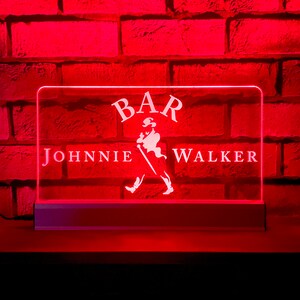 May include: A white neon sign with the words "BAR" and "JOHNNIE WALKER" against a red brick background.