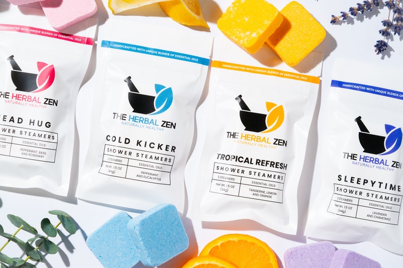 May include: Four white pouches with different colored shower steamers. Each pouch has a black and white mortar and pestle logo with the text "The Herbal Zen Naturally Healthy". The pouches are labeled "Head Hug", "Cold Kicker", "Tropical Refresh", and "Sleepytime".