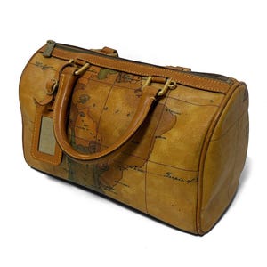 May include: A tan leather duffel bag with a world map design. The bag has brown leather handles, a zipper closure, and a luggage tag. The bag is cylindrical and has a vintage aesthetic.