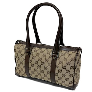 May include: A brown and tan handbag with a repeating pattern of interlocking Gs. The bag has two dark brown handles and matching trim. The bag is rectangular with a zipper closure.
