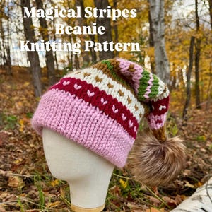 Peut inclure: Un bonnet tricoté rose, blanc, rouge et vert avec un pompon en fausse fourrure marron. Le chapeau est présenté sur une tête de mannequin. Le texte "Magical Stripes Beanie Knitting Pattern" est visible.