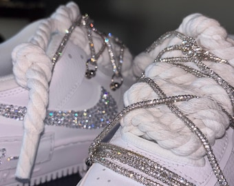 Puede incluir: Zapatillas blancas con detalles de pedrería en el logotipo de Nike y alrededor de los cordones. Los cordones se reemplazan con una cadena plateada brillante. Los zapatos tienen cordones gruesos de cuerda blanca.
