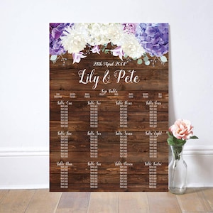 May include: A rustic wooden wedding seating chart with purple and white flowers. The chart lists tables one through twelve, with space for guest names. The date "28th April 2018" and the names "Lily & Pete" are written at the top.